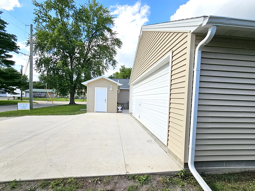 Exterior view on South side of property showing part of the driveway, garage, the back door to the house, and the breezeway leading to the private patio area